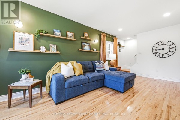 Living room facing a blue sectional sofa, light wood floors, and a large wall clock. - 255 Weir Street N, Hamilton