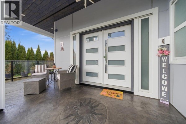 Covered patio with two red chairs, a coffee table, and a glass railing overlooking a landscaped backyard. - 25507 Bosonworth Avenue, Maple Ridge