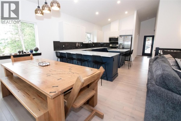 Spacious open-concept living area featuring a large wooden dining table, a U-shaped kitchen island with seating, and white cabinets. - 2552 Sandstone Mews, Invermere