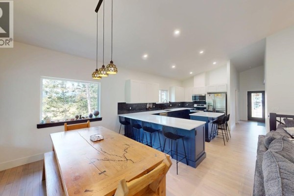An expansive open-concept room showcases a dining area, a modern kitchen with a navy island, and a living area with a sofa. - 2552 Sandstone Mews, Invermere