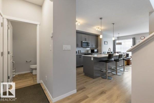 View of a modern kitchen with grey cabinets, island, and stools, adjacent to a half bathroom. - 2554 151a Av Nw, Edmonton