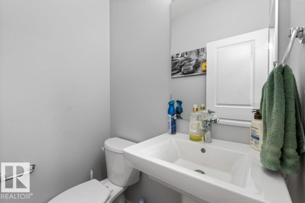 A modern half bathroom with a white pedestal sink, toilet, and mirror. - 2554 151a Av Nw, Edmonton