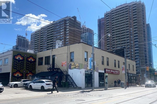 View of commercial building and parking area with residential towers in background. - 2558 Danforth Avenue, Toronto