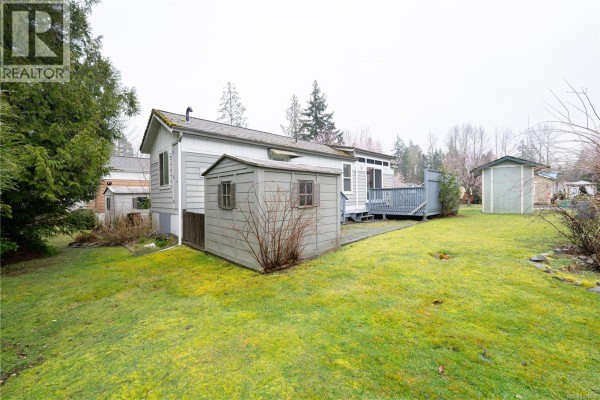 Rear yard view showing mobile home, storage shed, and green lawn - 256 3042 River Rd, Chemainus