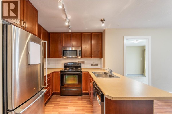 Kitchen area featuring dark wood cabinetry, stainless steel appliances, and laminate flooring. - 256 Hastings Avenue Unit# 203, Penticton