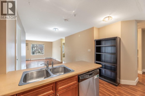 View of the open-concept living area and kitchen, with a bookshelf on the right. - 256 Hastings Avenue Unit# 203, Penticton