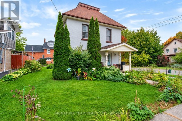 Side view of a two-story white brick house with a pitched roof and mature trees. - 256 Maple Avenue, Pembroke