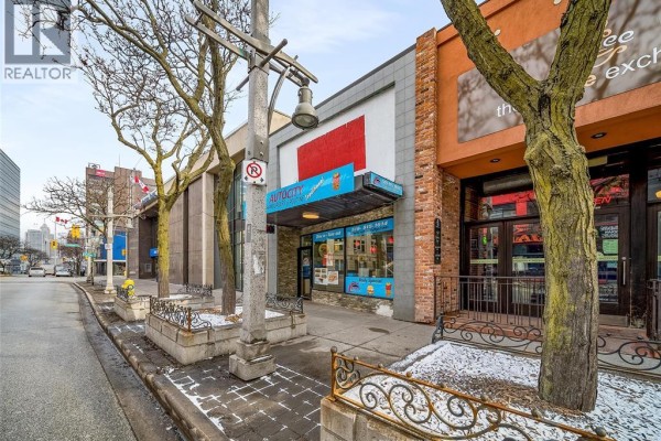 View of Autocity storefront from the street with trees and utility pole. - 256 Ouellette Avenue, Windsor