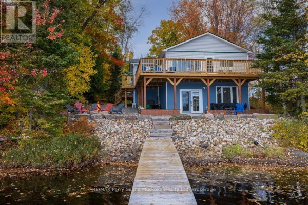 House exterior with blue siding, wooden deck, and stone landscaping leading to a dock. - 256 Tahinca Road, Whitestone
