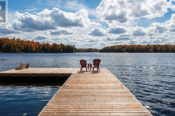 Wooden dock with two red chairs facing a wide blue lake under a cloudy sky. - 256 Tahinca Road, Whitestone
