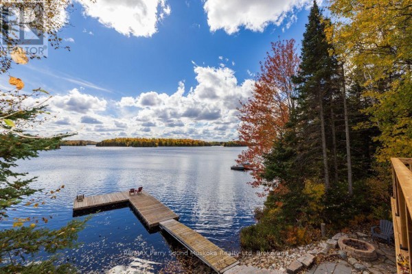 Lake view from the property, showing a dock with chairs and surrounding trees in fall. - 256 Tahinca Road, Whitestone