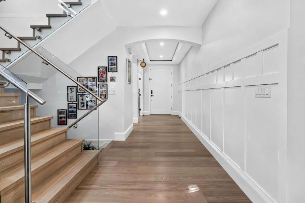 Wide entryway with light wood floors, white wainscoting, and a glass-railed staircase. - 2560 163 Street, Surrey