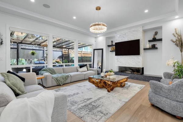 Living room with a sectional sofa, fireplace, television, and large windows looking onto a backyard patio. - 2560 163 Street, Surrey