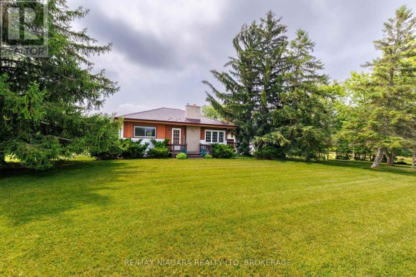 Side view of a house surrounded by green lawn and tall evergreen trees. - 2561 Point Abino Road N, Fort Erie