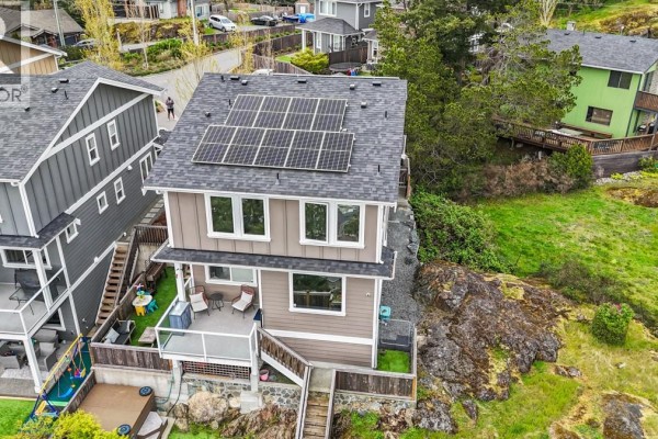 Rear exterior of a brown house with a deck, glass railing, and rock landscaping. - 2562 Rosevista Pl, Langford