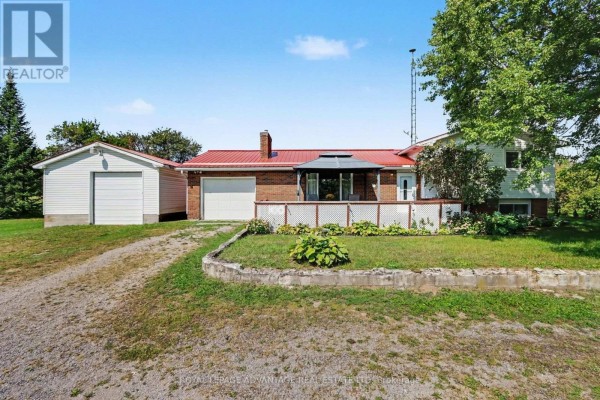 View of the brick house from the side, showing green lawn and trees. - 2564 2nd Conc Road, Augusta
