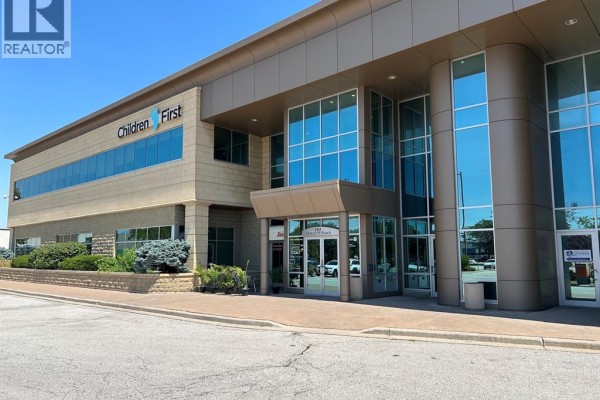Exterior view of a modern commercial building with glass windows, tan siding, and signage for 'Children First'. - 2565 Ouellette Avenue Unit# 300, Windsor