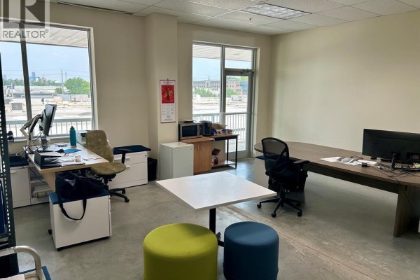 Office space with large windows, two desks with computers, a conference table, and colorful ottomans on concrete floors. - 2565 Ouellette Avenue Unit# 300, Windsor