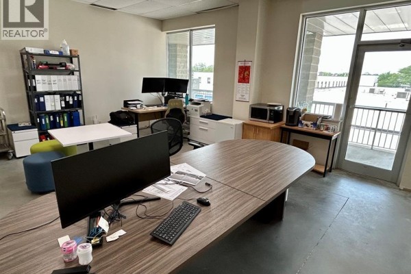 Office interior with desks, computers, filing cabinets, storage shelves, and a glass-doored exit leading to a balcony. - 2565 Ouellette Avenue Unit# 300, Windsor