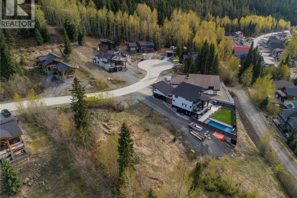 A winding road cuts through a snowy mountain neighborhood with contemporary homes and dense evergreen forest. - 2568 Mountain View Drive Lot# 12, Sun Peaks