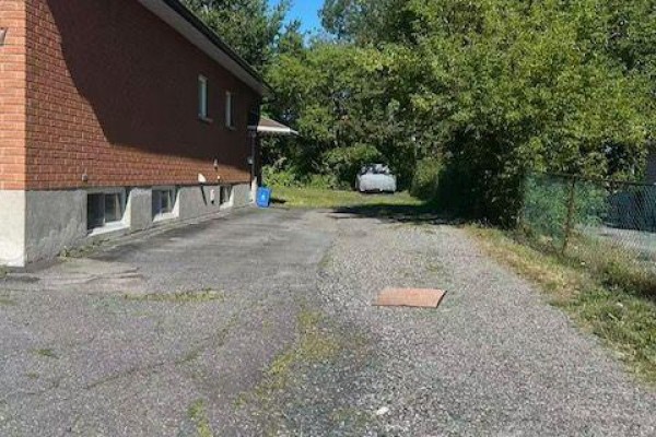 Paved driveway leading to the backyard with trees and a chain-link fence. - 257 Leslie Street, Greater Sudbury