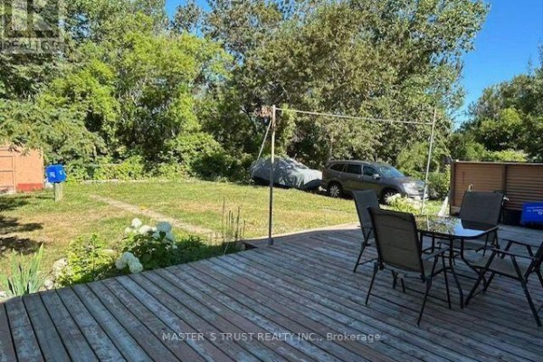 Wooden deck with chairs and a table overlooking a green backyard with cars. - 257 Leslie Street, Greater Sudbury