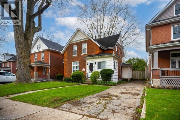 Side view of a red brick house with white siding, a driveway, and a fenced backyard. - 257 Ontario Street, Stratford