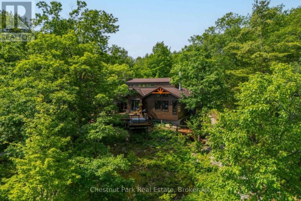 View of the Georgian Bay home nestled amongst trees, with a wooden deck. - 257 Sweets Portage Road, Georgian Bay