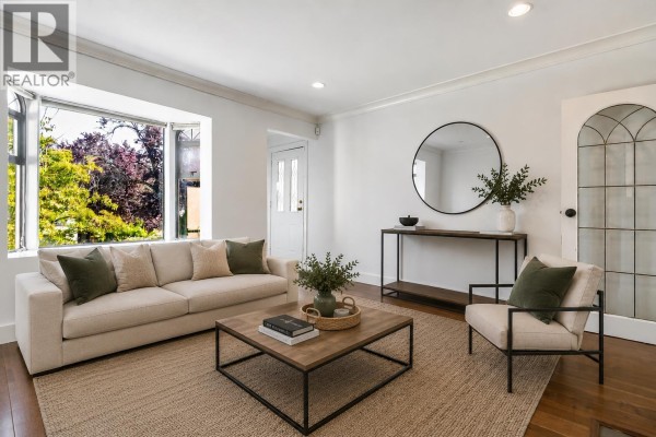 Living room with a large bay window, sofa, armchair, coffee table, and wood flooring. - 2576 Parker Street, Vancouver