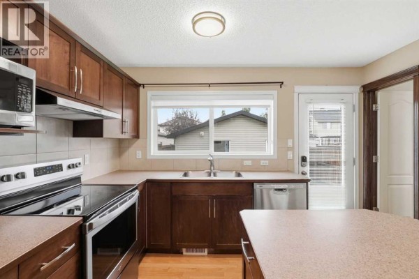 View of the living room, stairs, and kitchen area with an island and stainless steel appliances. - 258 Cranberry Place Se, Calgary