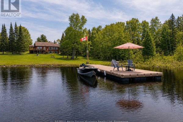 Side view of the orange house with a sloped roof, green lawn, and trees in the background. - 258 Lakeside Trail, Magnetawan