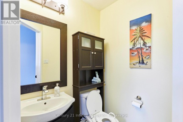 Powder room with a white sink, dark brown vanity, toilet, and a tropical wall painting. - 258 Swindells Street, Clarington