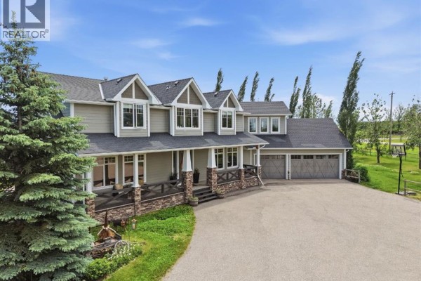 Front view of a large, light green house with a wide covered porch, stone pillars, and a three-car garage. - 258244 10 Street E, Rural Foothills County