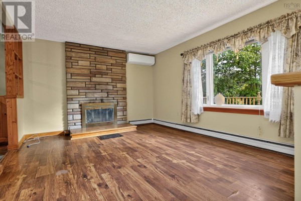 Living room with a stone fireplace, wood floors, and a large bay window. - 2587 Sackville Drive, Upper Sackville