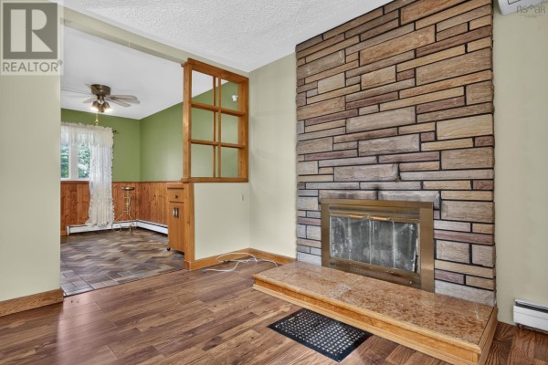 Living room with stone fireplace, wood floors, and view into a green room. - 2587 Sackville Drive, Upper Sackville