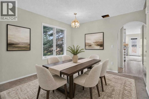 A dining room with a wooden table, upholstered chairs, and a large window. - 259 Coachway Road Sw, Calgary
