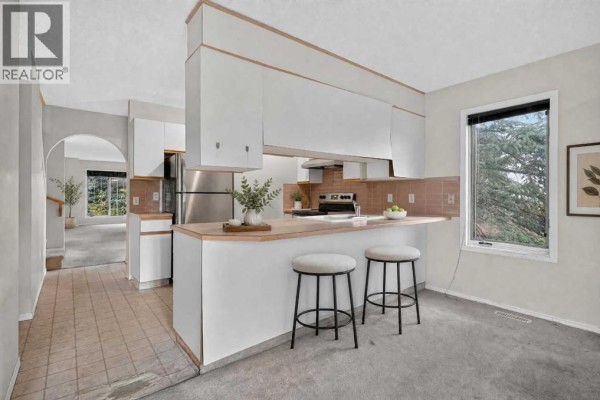 A kitchen with white cabinets, stainless steel appliances, and a breakfast bar with stools. - 259 Coachway Road Sw, Calgary