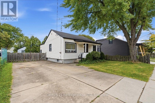 Side view of the bungalow showing the driveway, lawn, and adjacent properties. - 26 Coventry Street, St  Catharines