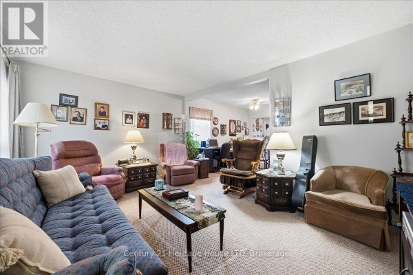Living room with beige carpet, blue sofa, upholstered chairs, and wooden furniture. - 26 Coventry Street, St  Catharines
