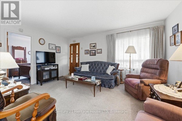 Living room with a blue sofa, upholstered chairs, television, and doorway to another room. - 26 Coventry Street, St  Catharines