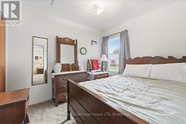 Bedroom with a large wooden bed, dresser, mirror, and a window with grey curtains. - 26 Coventry Street, St  Catharines