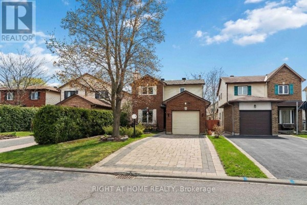 Front view of a two-story brick house with a garage, paved driveway, and neat landscaping. - 26 Denham Way, Ottawa