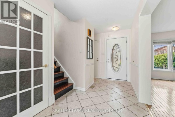 Interior entryway with cream-colored tile flooring, a staircase with wood treads, and a decorative glass front door. - 26 Denham Way, Ottawa