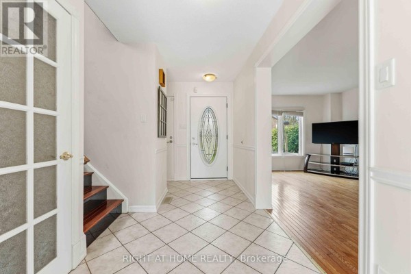 Entryway featuring cream tile floors, a staircase with dark wood treads, leading into a living area with wood floors. - 26 Denham Way, Ottawa