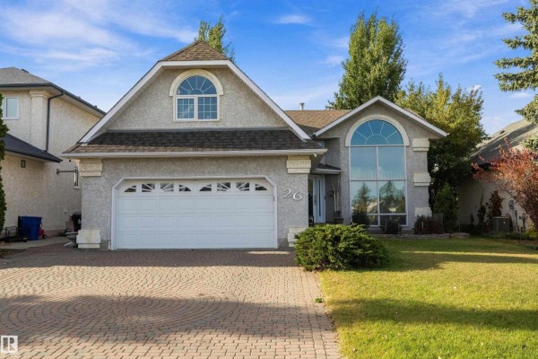 Front view of a light-colored stucco house with a double garage and large arched windows. - 26 Fairway Dr, Spruce Grove