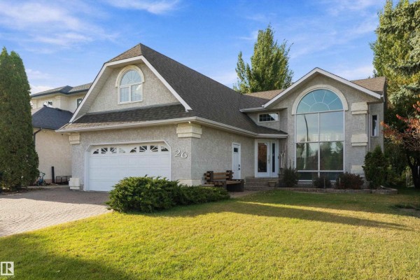 Front facade of a stucco house with a manicured lawn, paved driveway, and mature trees. - 26 Fairway Dr, Spruce Grove