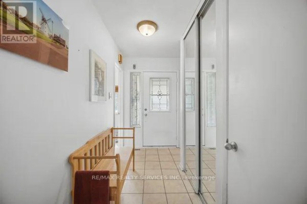 Bright entryway with tiled floor, wooden bench, and a glass-paned front door. - 26 Fanshawe Drive, Brampton