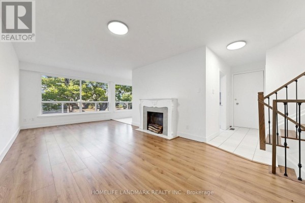 Living room with fireplace, large window overlooking trees, and entrance staircase. - 26 Fenside Drive, Toronto