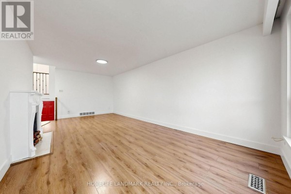 Living room with hardwood floors, fireplace, and red door leading to staircase. - 26 Fenside Drive, Toronto