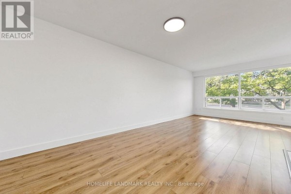 Living room with large window overlooking trees and hardwood floors. - 26 Fenside Drive, Toronto